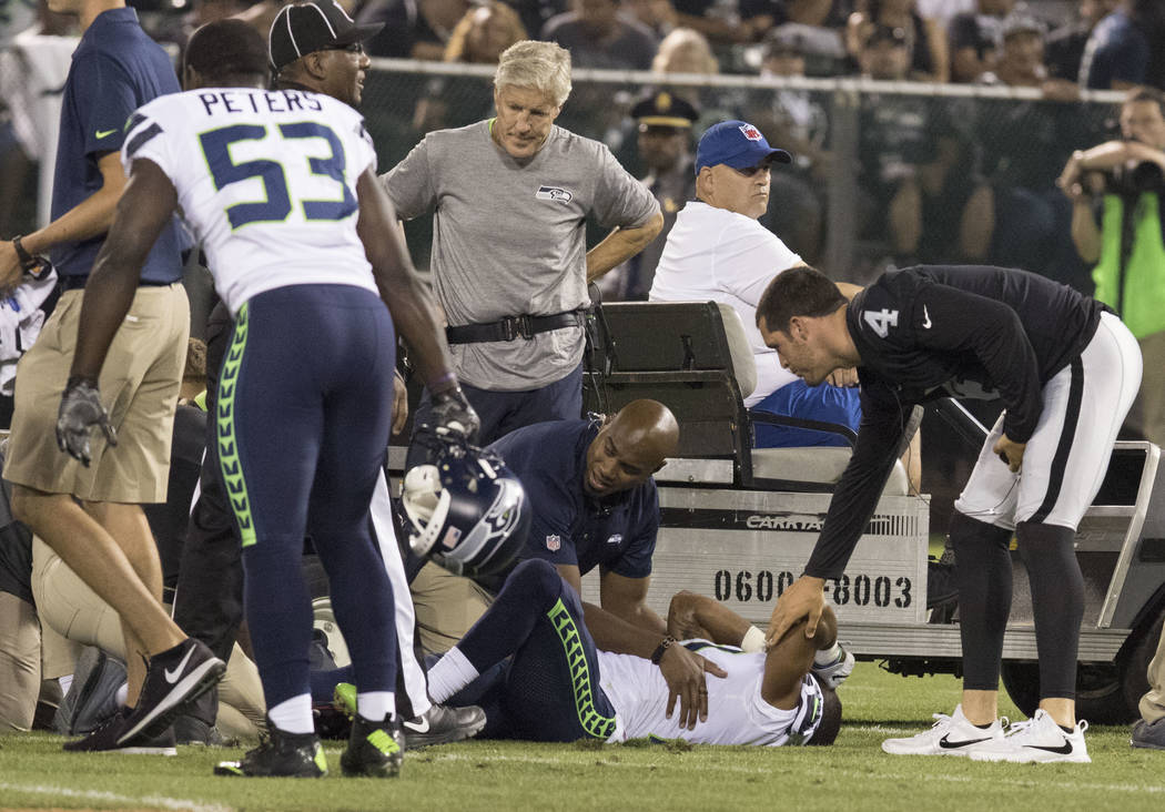 Seattle Seahawks cornerback DeAndre Elliott (21) is hurt after a play as Oakland Raiders quarterback Derek Carr (4) comes to comfort him in the first half of the preseason game in Oakland, Calif., ...