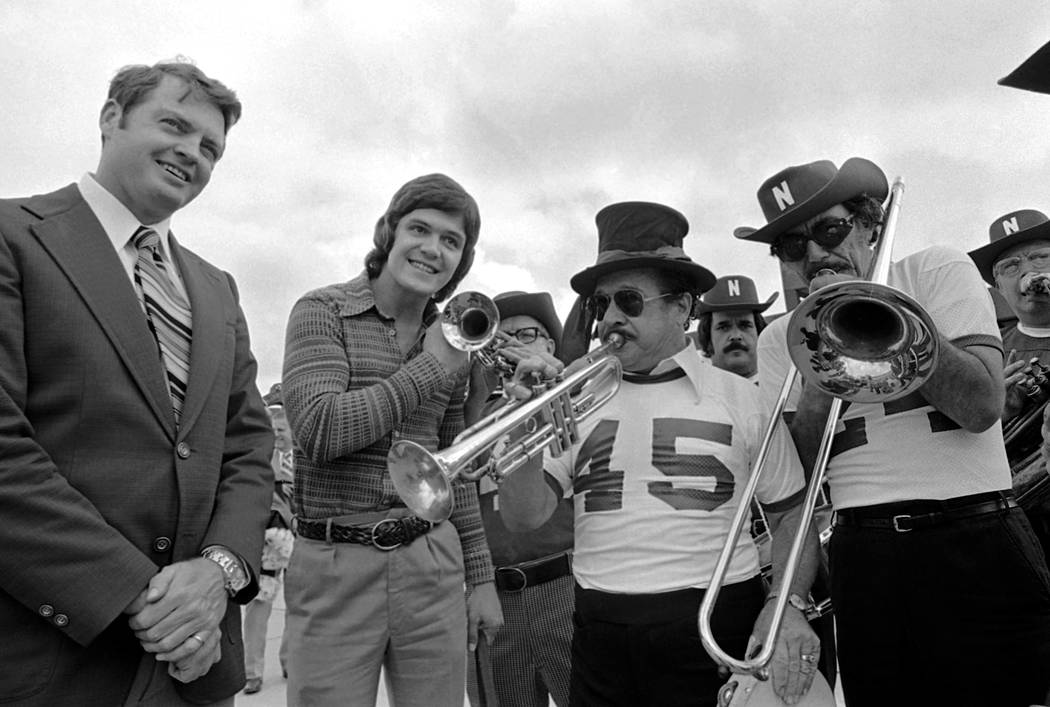 Nebraska quarterback Dave Humm is flanked by his head coach Tom Osborne as they listen to a dixieland jazz band greeting upon arrival in New Orleans on Tuesday, Dec. 24, 1974. The 8th ranked Cornb ...