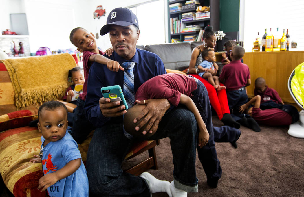 Deon Derrico checks his phone while sitting with his children, from left, Dior, 1, Deniko, 4, a ...