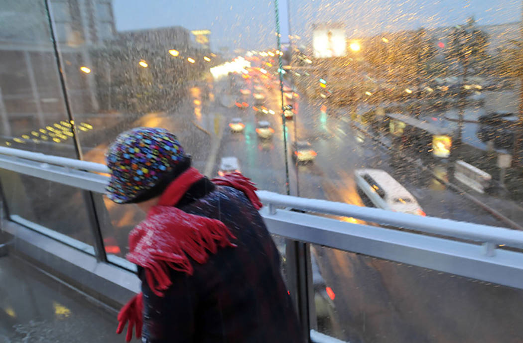 A woman bundled up braves the freezing rain and snow as she crosses one of the pedestrian bridg ...