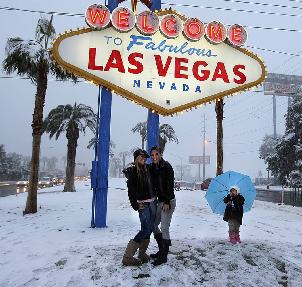 Visitors have their picture taken at the welcome sign during a snowstorm on the Las Vegas Strip ...