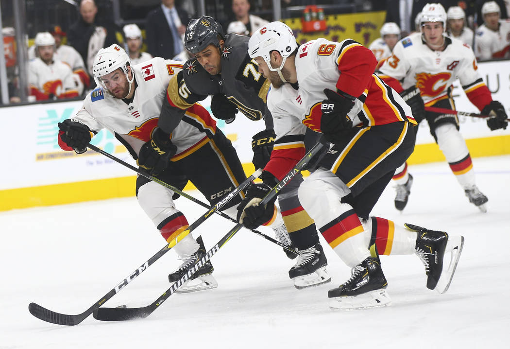 Golden Knights right wing Ryan Reaves (75) battles to keep control of the puck against Calgary Flames defensemen TJ Brodie (7) and Dalton Prout (6) during the first period of an NHL hockey game at ...