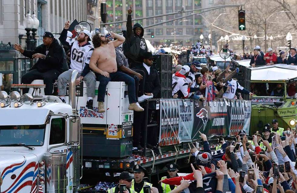 New England Patriots' Trent Brown, left, and Joe Thuney, center, sit beside David Andrews as he chugs a beverage during the team's parade through downtown Boston, Tuesday, Feb. 5, 2019, to celebra ...