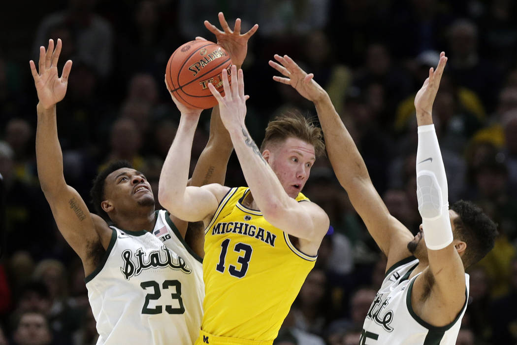 Michigan's Ignas Brazdeikis (13) looks to pass the ball against Michigan State's Xavier Tillman (23) and Kenny Goins (25) during the first half of an NCAA college basketball championship game in t ...
