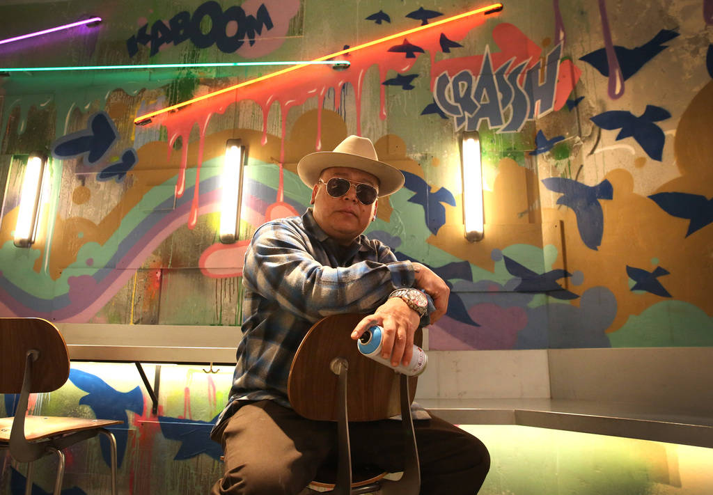 Tiki Jay One, an Urban Landscapist/Commercial Designer, poses for a photo in front of the mural ...