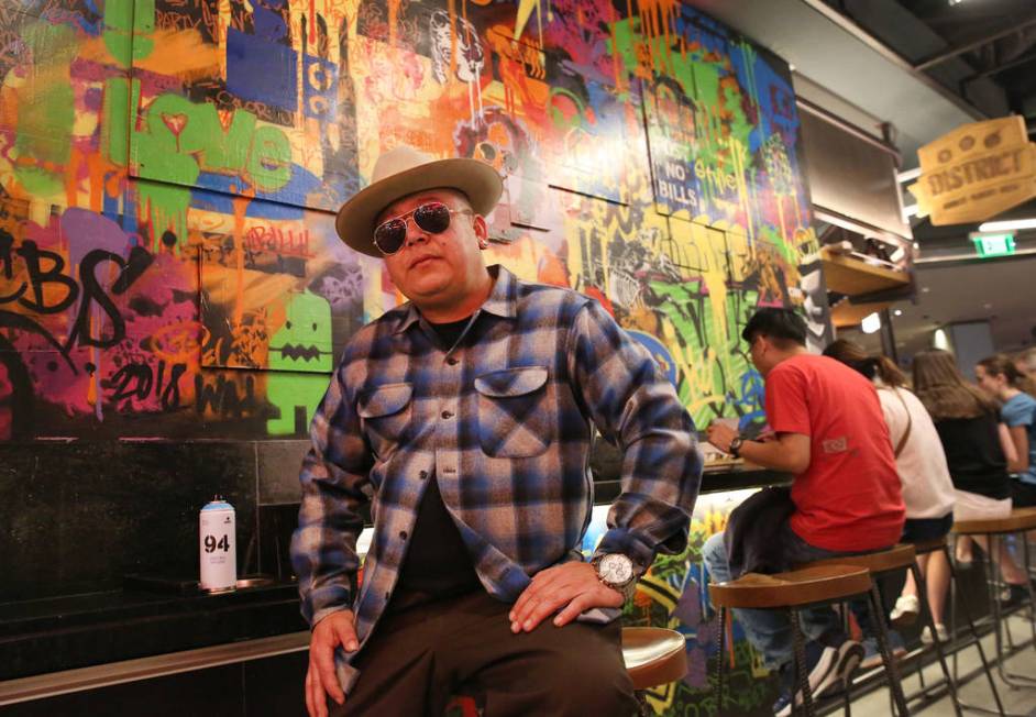 Tiki Jay One, an Urban Landscapist/Commercial Designer, poses for a photo in front of the mural ...