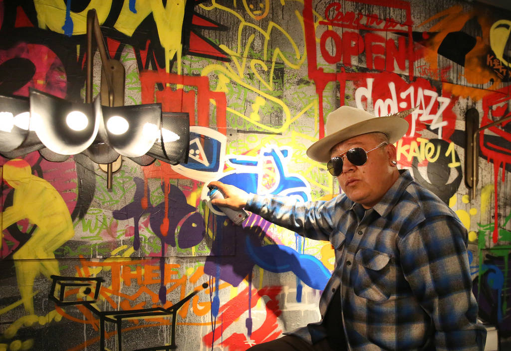 Tiki Jay One, an Urban Landscapist/Commercial Designer, poses for a photo in front of the mural ...