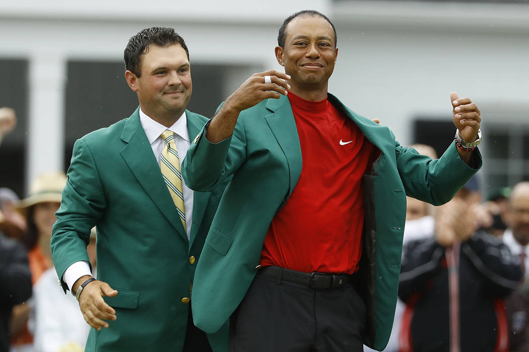 Patrick Reed helps Tiger Woods with his green jacket after Woods won the Masters golf tournamen ...