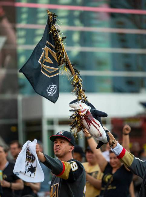A Golden Knights fan flies a flag with bloody shark attached while celebrating a goal with othe ...
