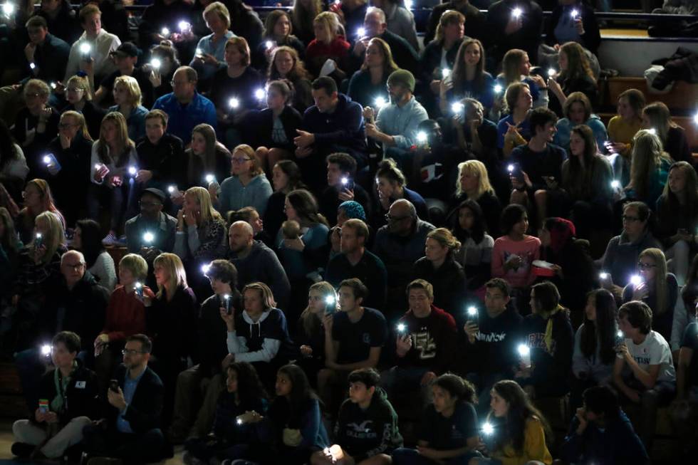 Attendees illuminate their mobile telephones during a community vigil to honor the victims and ...