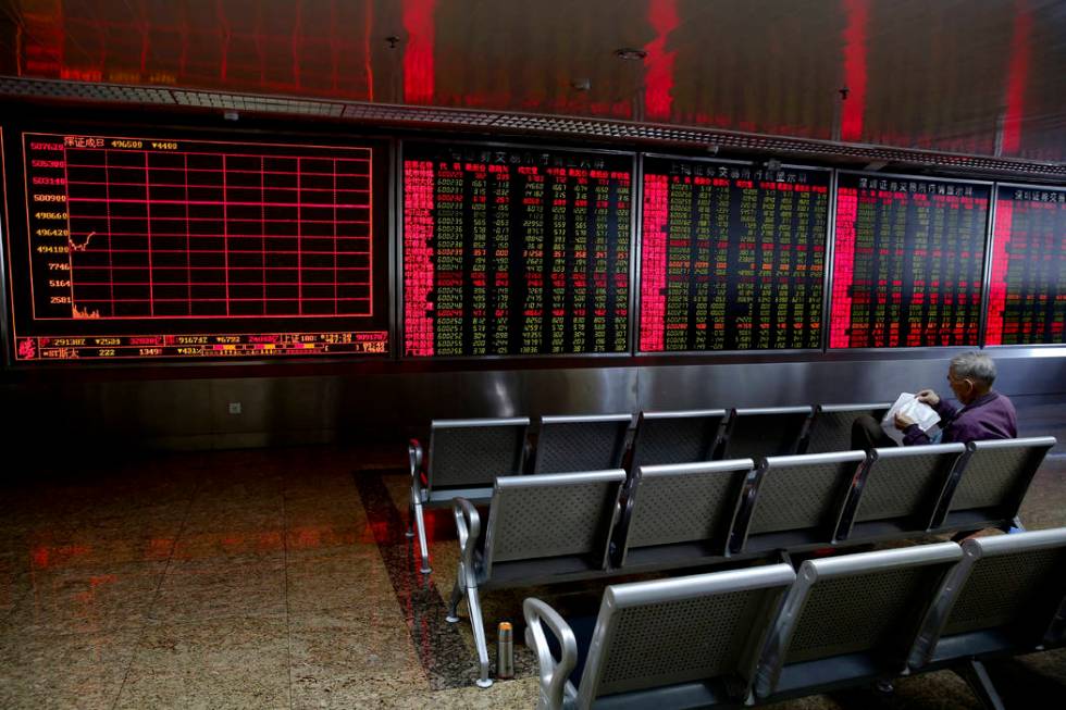 An investor looks at the stock marked on a paper as he monitors stock prices at a brokerage hou ...