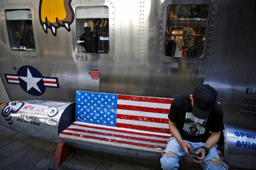 A man browses his smartphone on a bench with a decorated with U.S. flag outside a fashion bouti ...