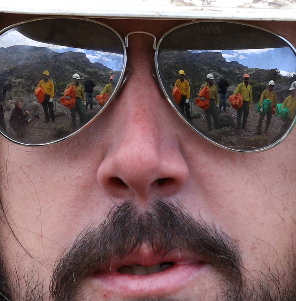 Firefighters from Bureau of Land Management are reflected in the sunglasses of Andrew Merriam, ...