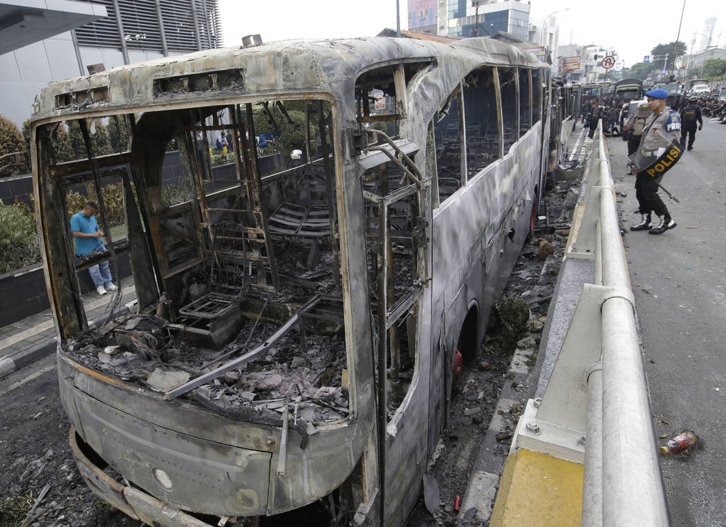 Indonesian police check burnt buses in Jakarta, Indonesia, Wednesday, May 22, 2019. Supporters ...