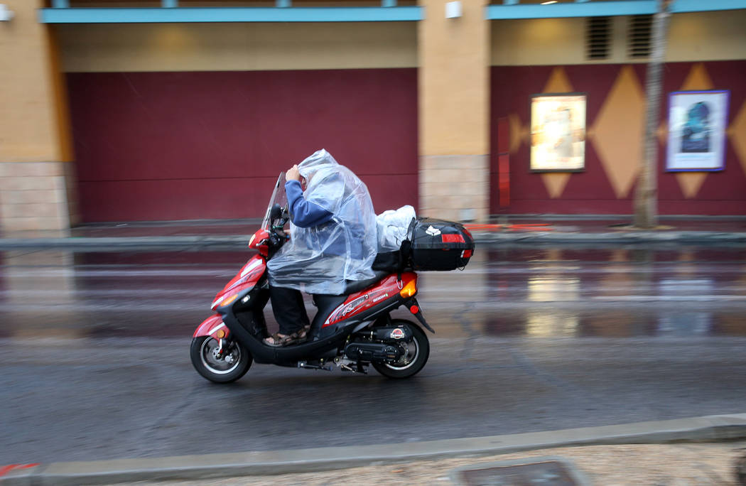 A scooter rider protects himself from a light rain on Las Vegas Boulevard near Fremont Street i ...