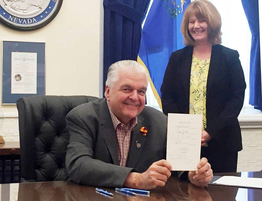 Nevada Gov. Steve Sisolak displays a bill he signed into law that opens the books on applicatio ...