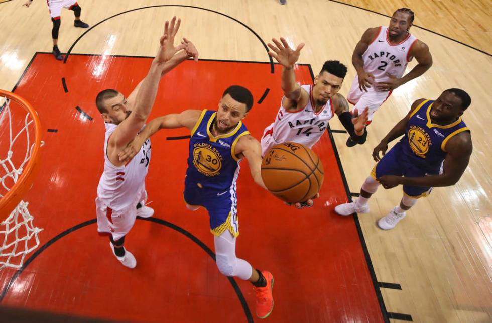 Golden State Warriors' Stephen Curry (30) drives to the basket between Toronto Raptors' Marc Ga ...