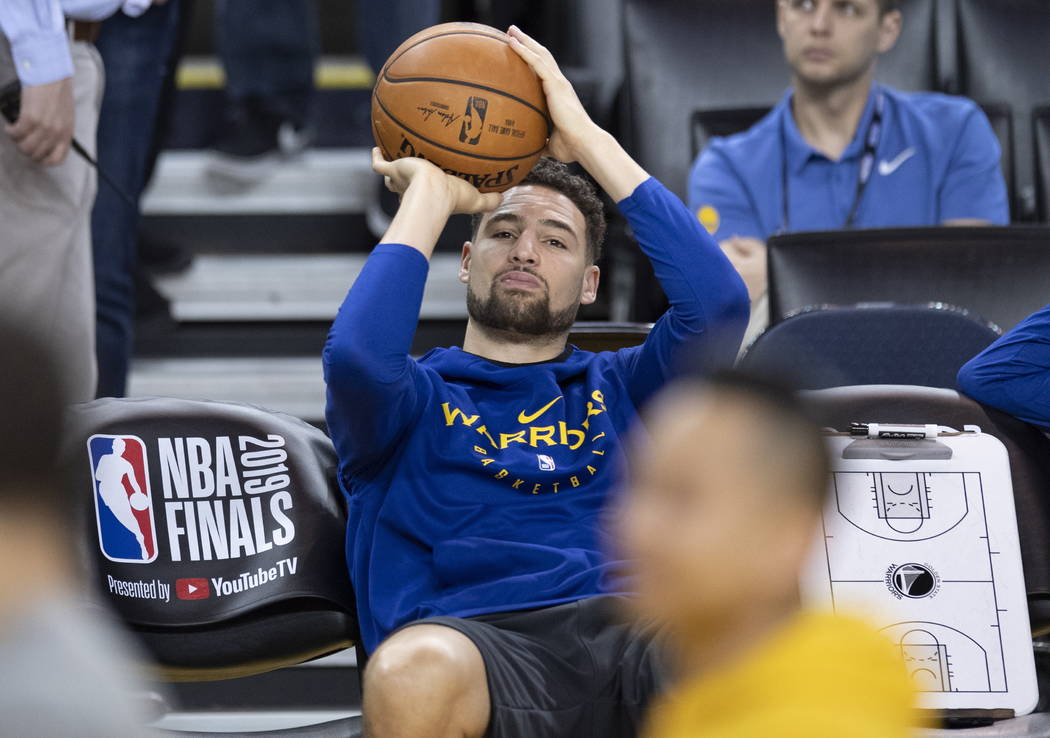 Golden State Warriors' Klay Thompson practices his shot motion as he sits on the bench watching ...