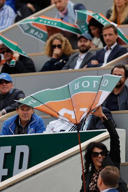 A spectator battles with her umbrella after the wind inverted it during the semifinal match of ...