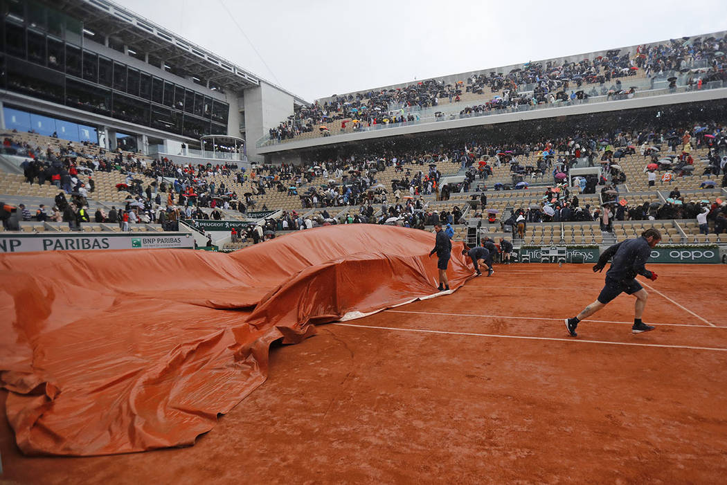 Workers run to cover center court as rain interrupted the men's semifinal match of the French O ...