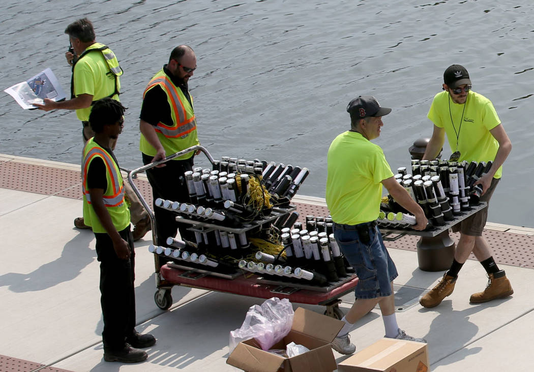 Workers move fireworks to barges on the Mystic River at Encore Boston Harbor in Everett, Mass., ...