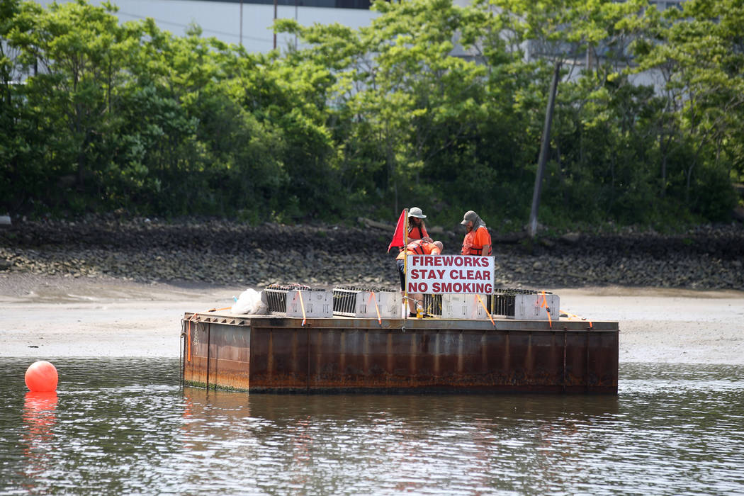 Workers prepare fireworks on barges on the Mystic River at Encore Boston Harbor in Everett, Mas ...