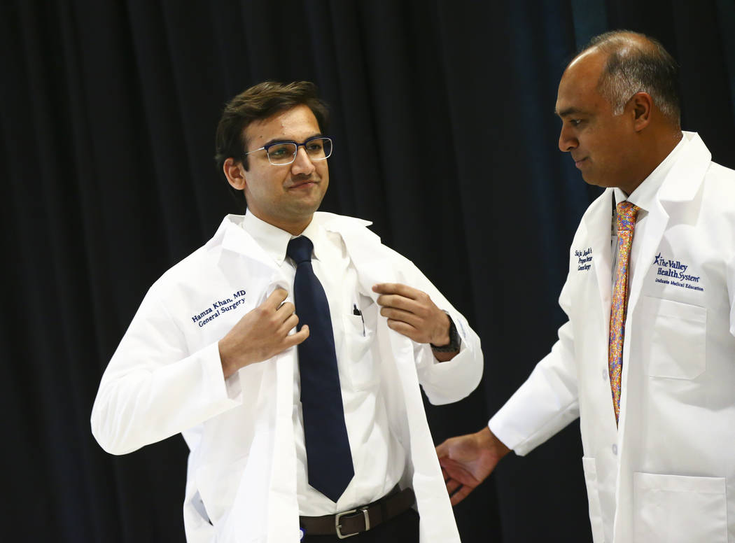General surgery resident Hamza Khan puts on his coat with the help of Saju Joseph, general surg ...