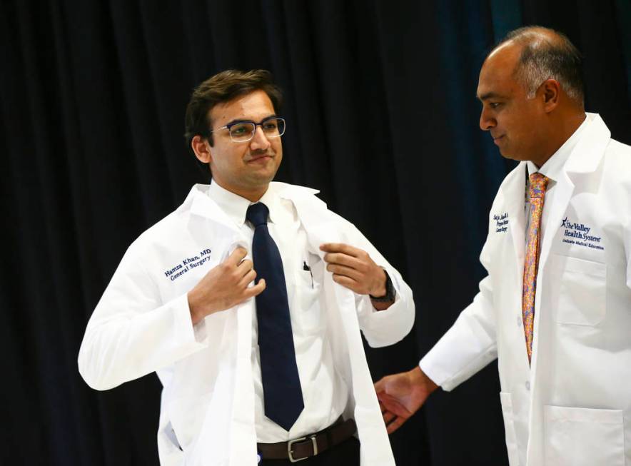 General surgery resident Hamza Khan puts on his coat with the help of Saju Joseph, general surg ...