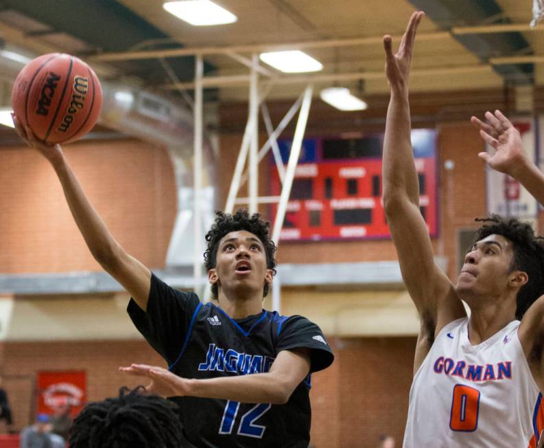 Desert Pines freshman Milos Uzan (12) splits Bishop Gorman junior forward Isaiah Cottrell (0 ...