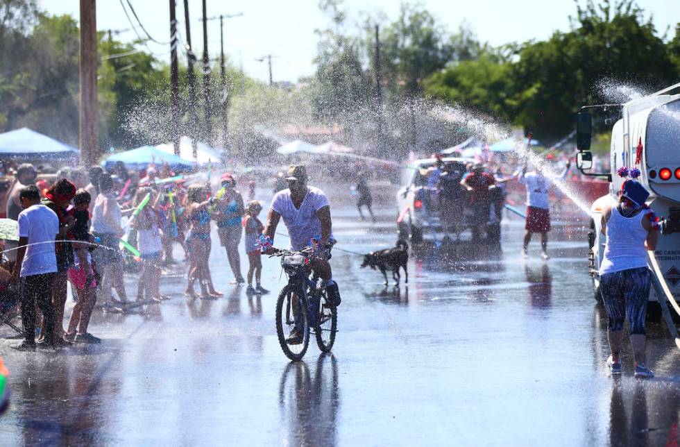 A man rides a bicycle as spectators and parade participants spray water during the parade at th ...