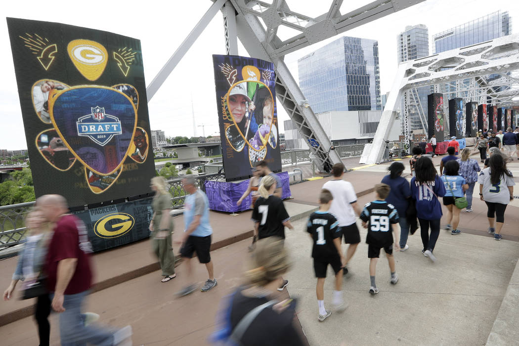 People walk on a bridge lined with video boards providing news on draft picks on the final day ...