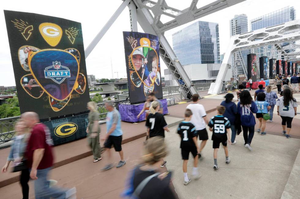 People walk on a bridge lined with video boards providing news on draft picks on the final day ...