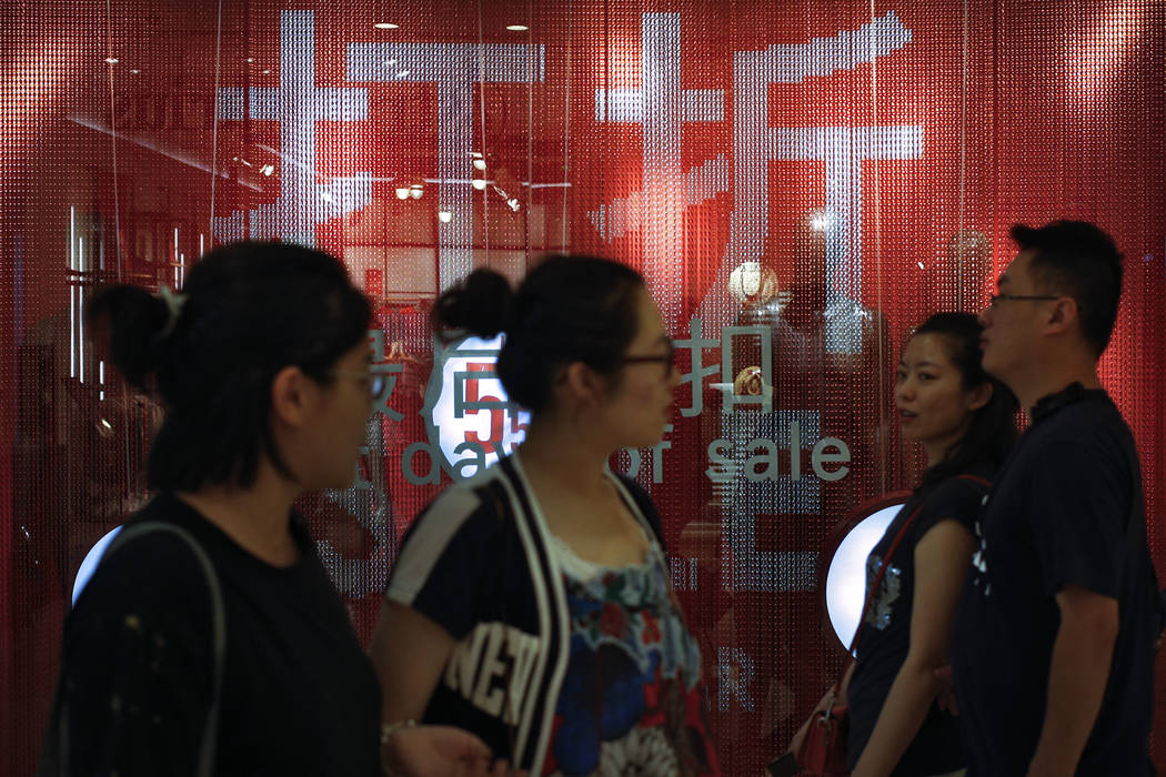 People walk by a fashion retailer having promotion sale at a shopping mall in Beijing, Monday, ...