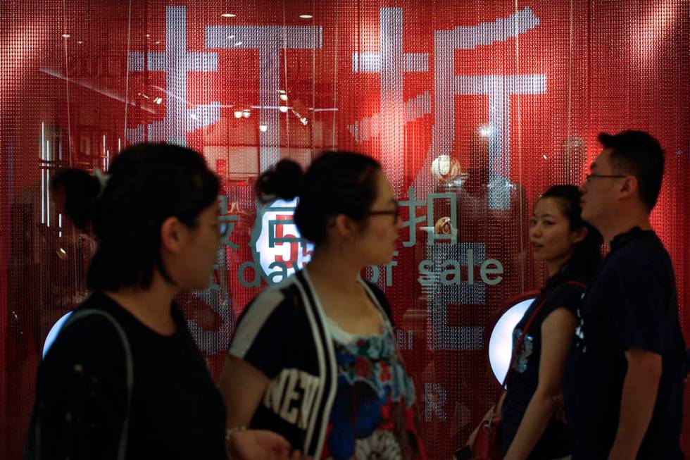 People walk by a fashion retailer having promotion sale at a shopping mall in Beijing, Monday, ...