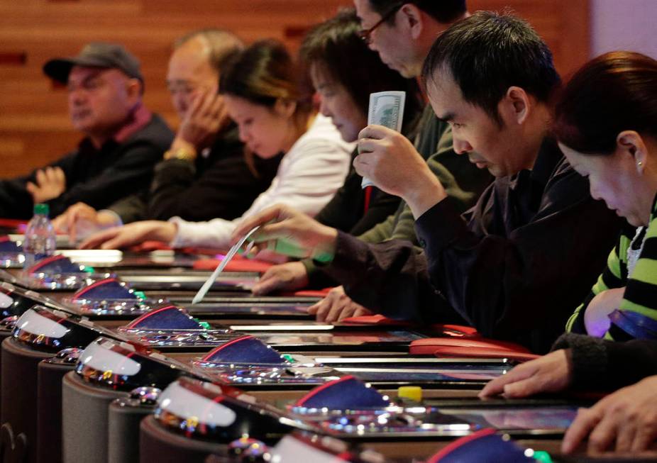 A gambler slides a $100 bill into an electronic baccarat game at the Resorts World Casino at th ...