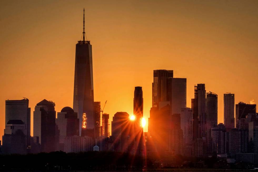 The sunlight flares around the buildings in lower Manhattan as the sun rises, Monday, July 1, 2 ...