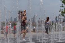 People enjoy the day playing in a water fountain as the Empire State Building is seen from Will ...
