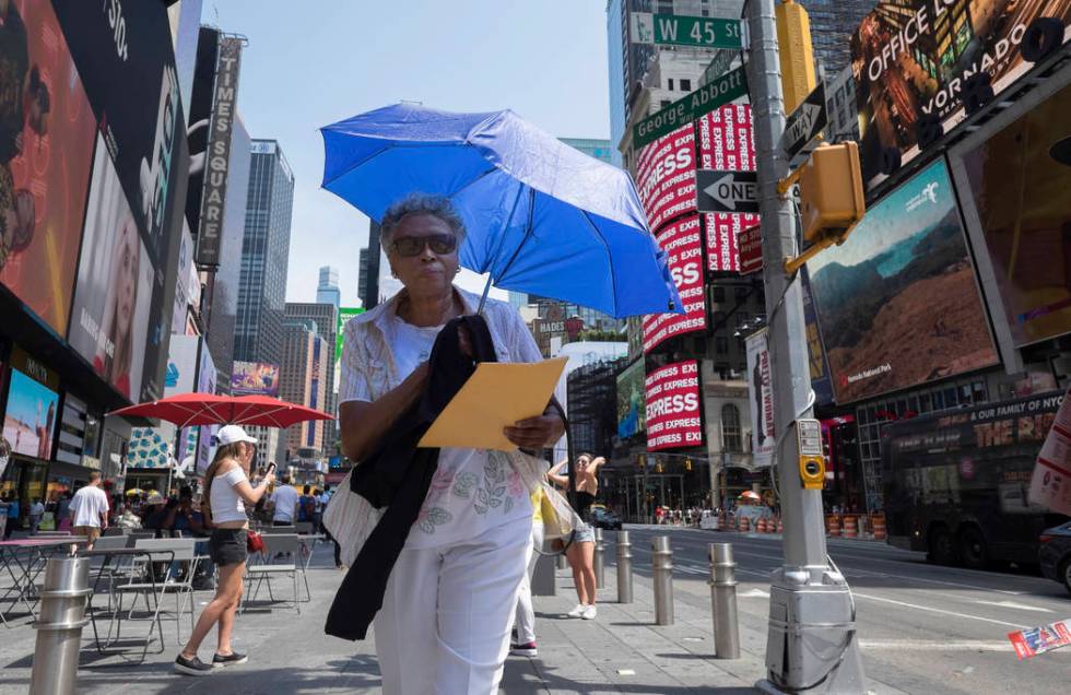 A woman uses an umbrella to block out the sun while walking through Times Square, Saturday, Jul ...
