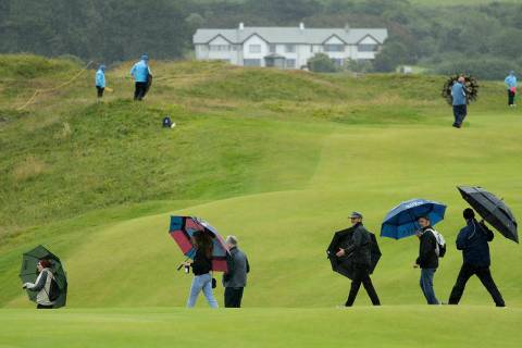 Spectators hold umbrellas as they cross the 15th hole in the rain as golfers practice ahead of ...