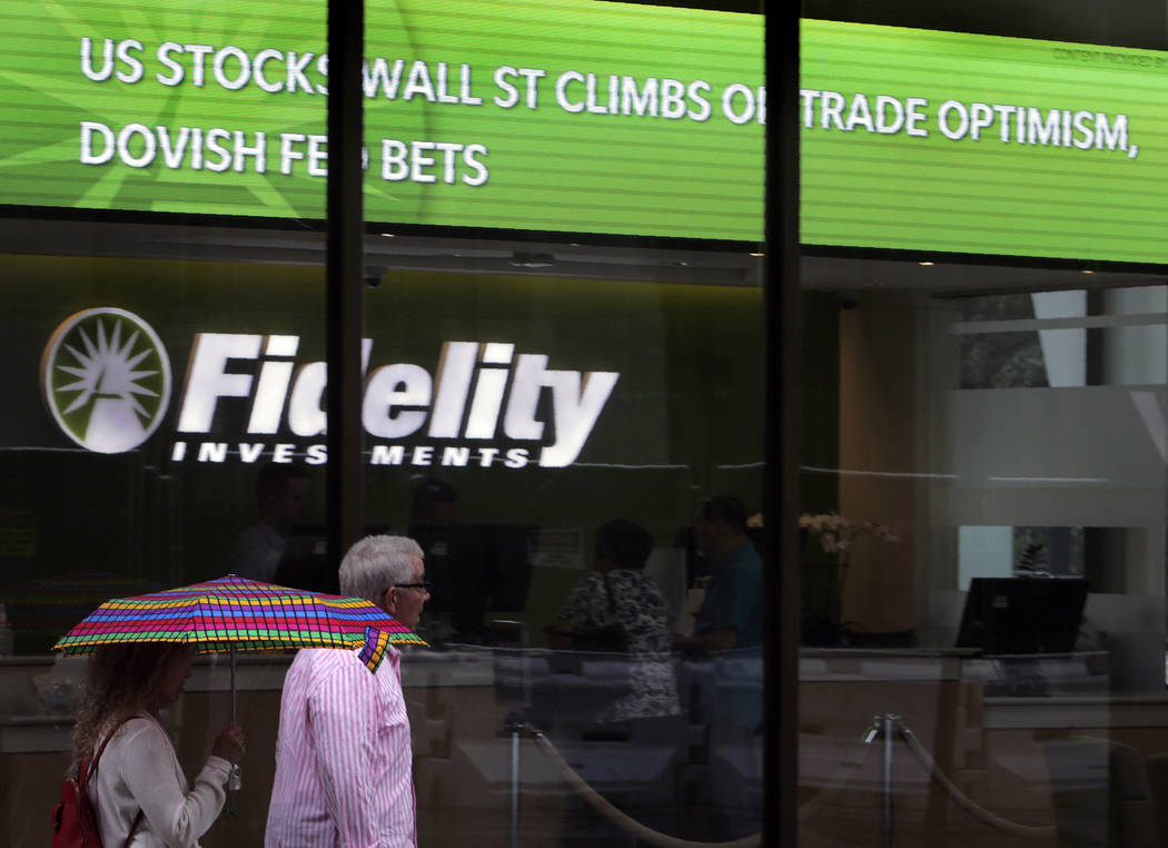 In this June 18, 2019, photo people walk past Fidelity Investments news scroll board, showing a ...