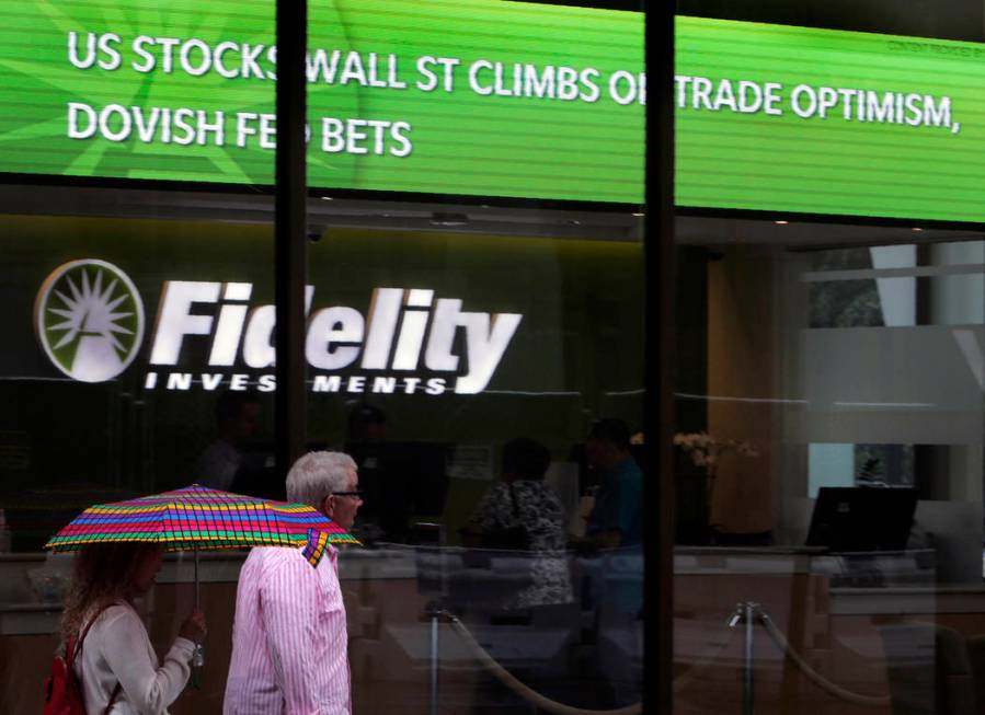 In this June 18, 2019, photo people walk past Fidelity Investments news scroll board, showing a ...