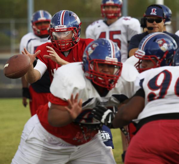 Liberty quarterback Tyler Newman, in red, reaches for the snap during practice.