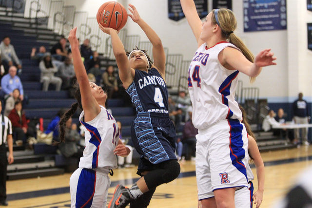 Canyon Springs guard Alize Bell drives between Reno guard Daranda Hinkey, left, and center M ...