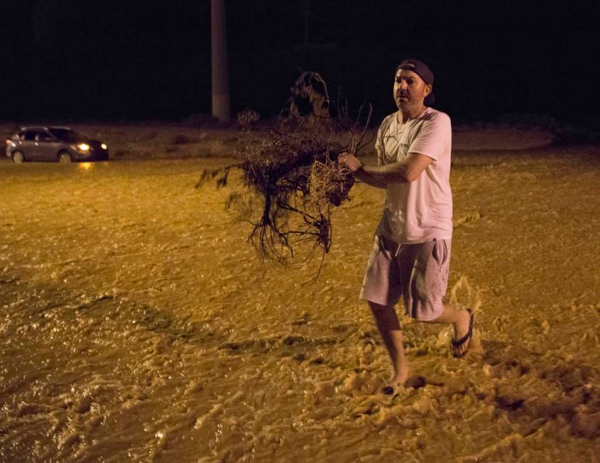 Jonathan Smedley runs through floodwaters with broken tree limbs to help his neighbors build a ...