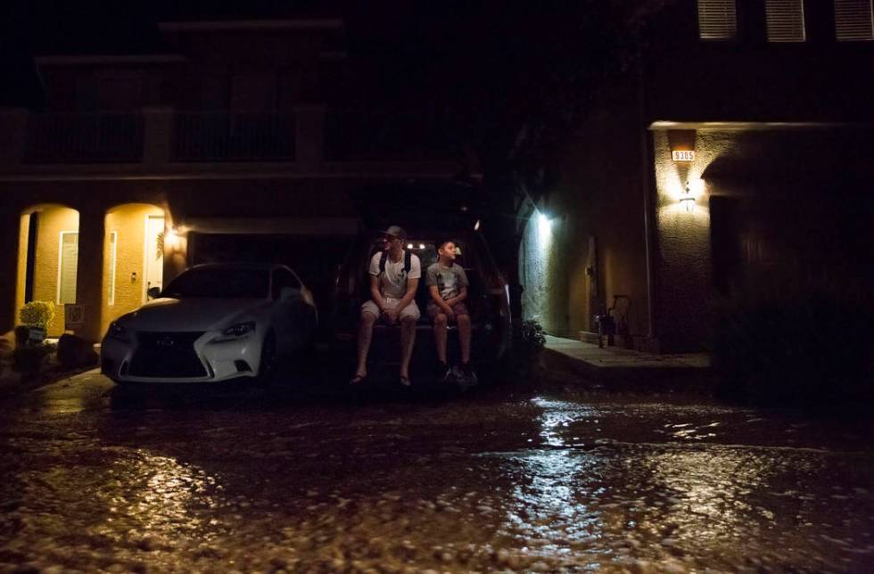 Jonathan Smedley, left, and son Cameron watch floodwaters flow past their home on West Fitzwill ...