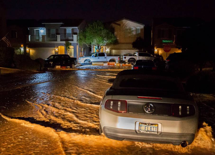 Floodwaters flow past vehicles and homes on West Fitzwilliam Avenue near South Fort Apache Road ...