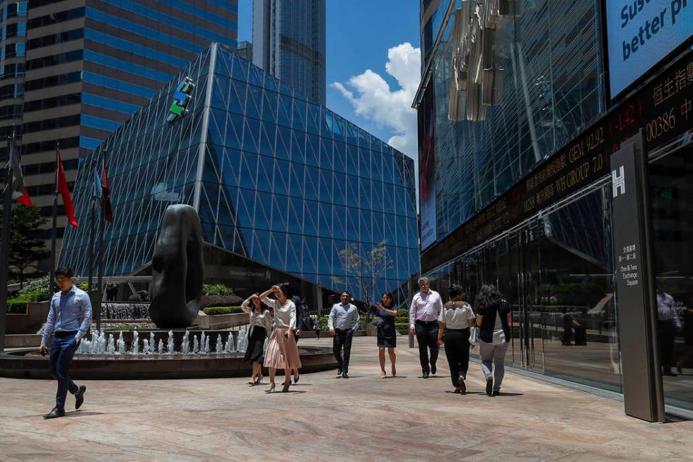 Office workers walk past an electronic board showing shares prices at the financial district in ...