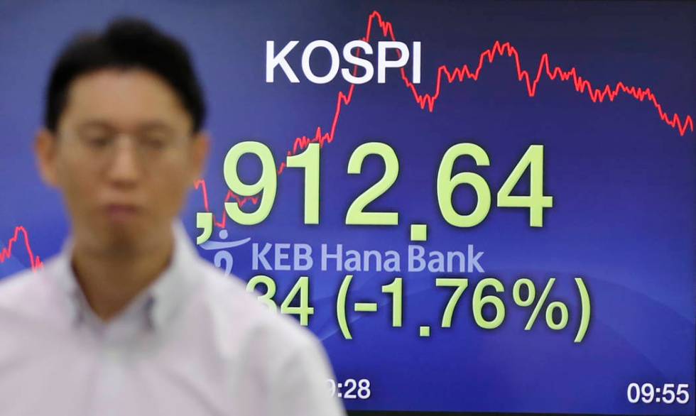 A currency trader walks by the screen showing the Korea Composite Stock Price Index (KOSPI) at ...