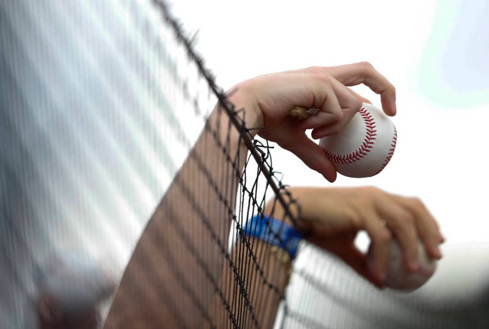 Fans hold baseballs over the protective netting before a spring training game between the New Y ...