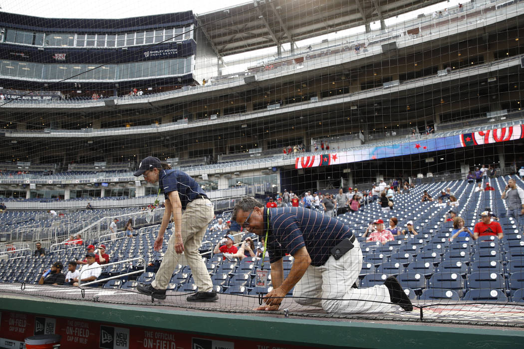 Workers adjust new netting that separates the infield from lower bowl seating before a basebal ...